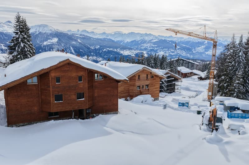 Two wooden chalets under construction with a beautiful snowy view of the mountains