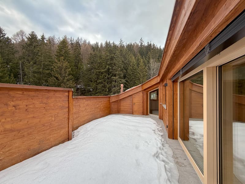 Wooden exterior with a curved terrace, covered in snow, panoramic view of the forest, large glass windows
