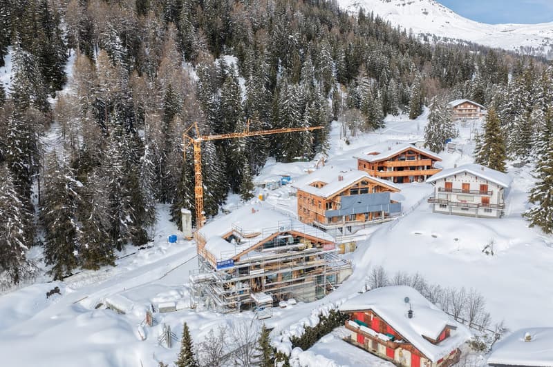 Buildings under construction in a snowy mountainous area, surrounded by trees.