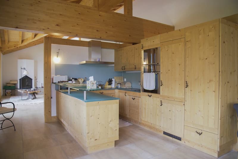 Open concept kitchen with wooden walls and ceiling, kitchen island with blue countertop, built-in appliances, and a fireplace in the background.
