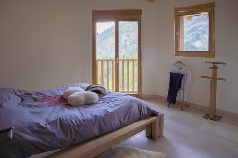 Spacious bedroom with large windows overlooking a scenic mountain landscape, wooden bed frame, plush bedding, and decorative pillows