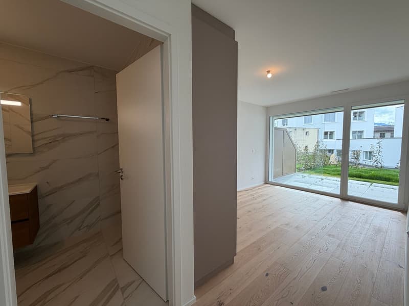 Empty room with wooden floor, white walls, large glass doors, and a view of the outside.