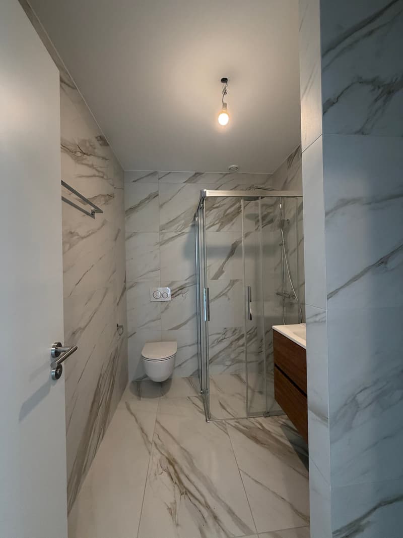 modern bathroom with white marble tiles, glass shower enclosure, white toilet, wooden vanity with sink, towel rack