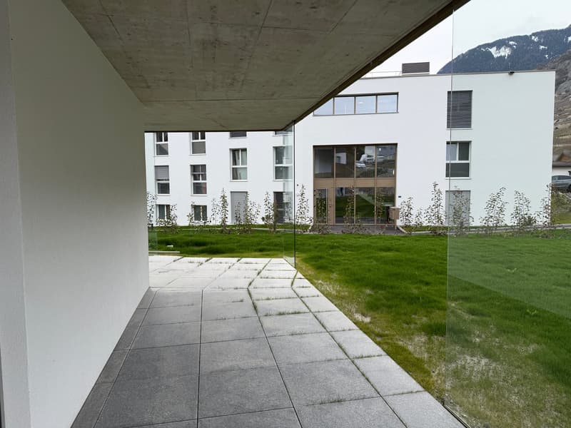 modern white building, glass walls, raised ground floor, concrete pathway, green lawn, mountain view