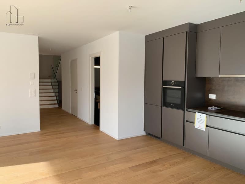 Empty room with wooden floor, white walls, gray cabinets, built-in oven, and a staircase leading to the upper floor.