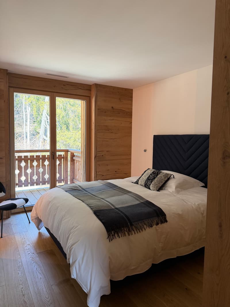 wooden floor, large bed, white bedding, wooden wall, balcony, view of trees