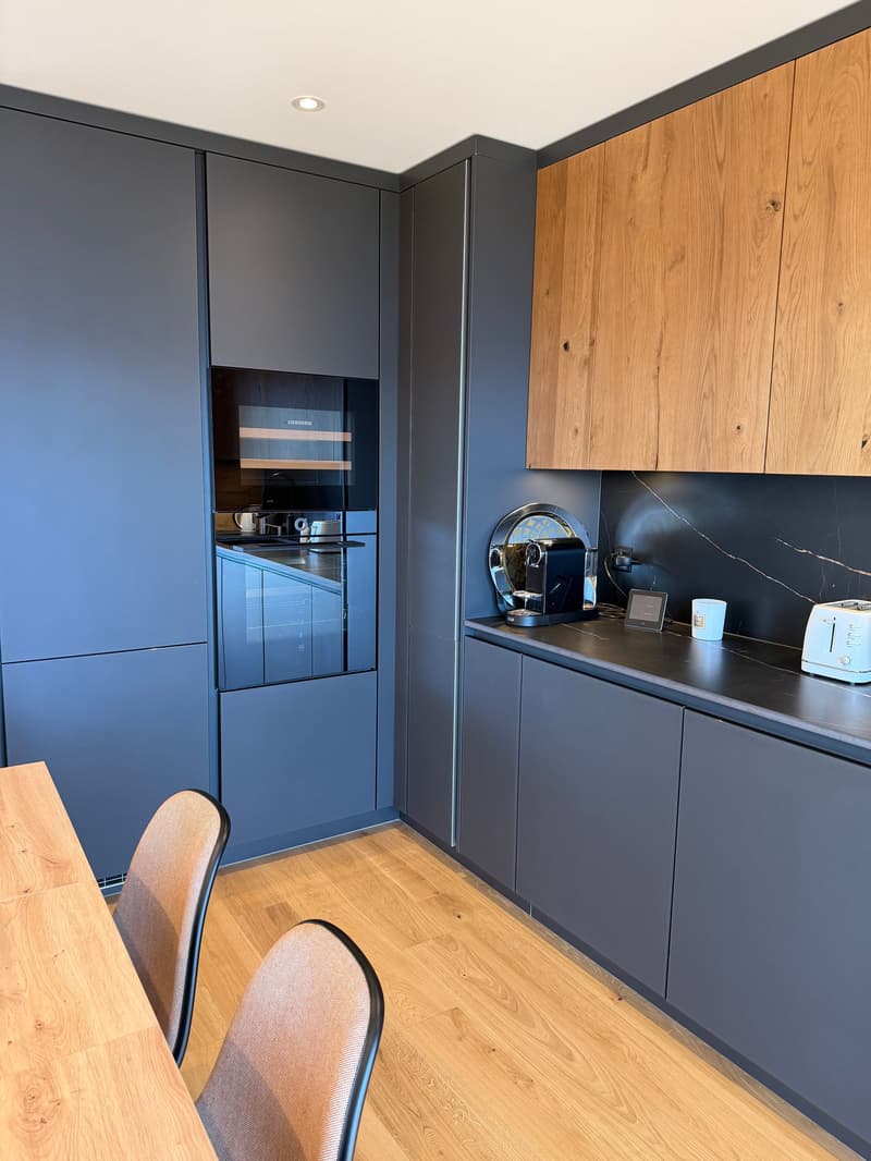 modern kitchen with wooden floor, blue cabinets, wooden countertops, built-in oven, coffee machine, toaster, and other kitchen appliances