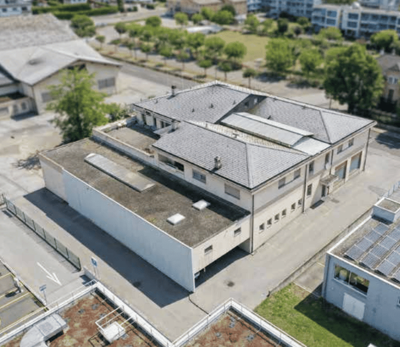 Aerial view of a large building with multiple windows, solar panels on the roof, and a parking area in front.