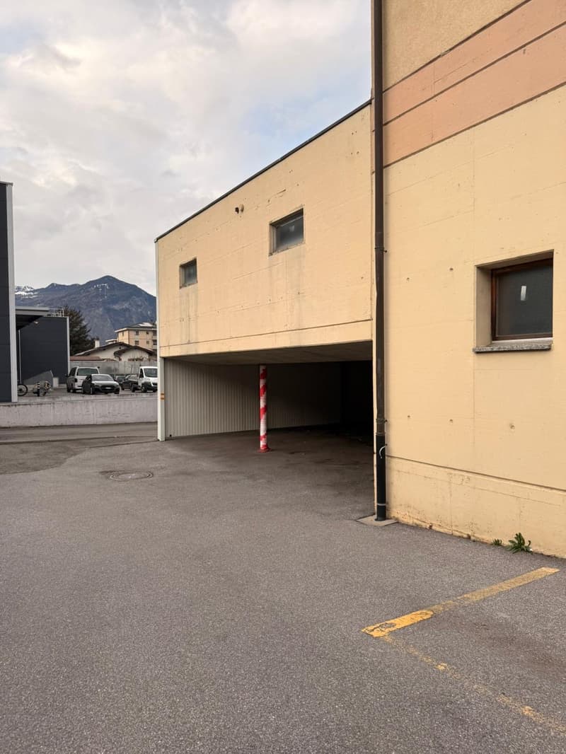 Building with a garage and parking lot, beige walls, red and white pole, mountains in the background