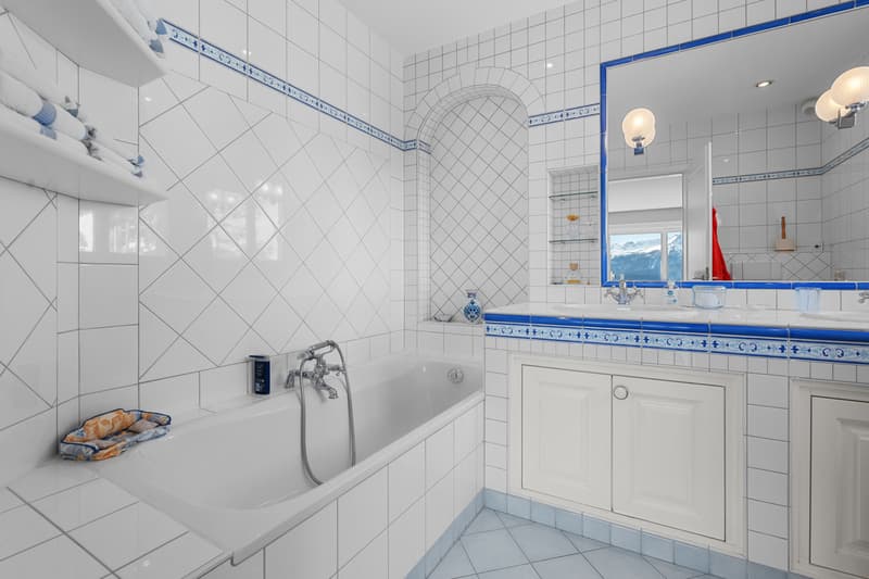 une salle de bains avec des carreaux blancs et bleus et un grand miroir au mur / a bathroom with white and blue tiles and a large mirror on the wall