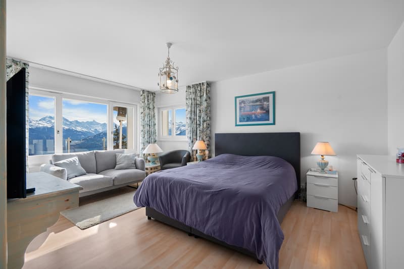 une chambre avec une grande fenêtre donnant sur les montagnes et un lit violet / a bedroom with a large window overlooking mountains and a purple bed