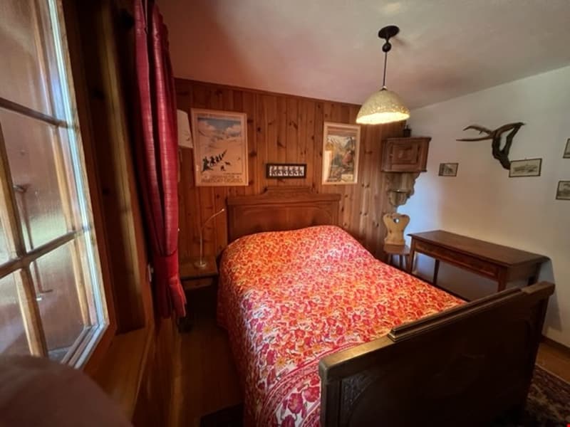 Cozy bedroom with wood-paneled walls, a large bed with a floral comforter, and a fireplace in the corner. There are also some framed artwork and decorative items on the walls.