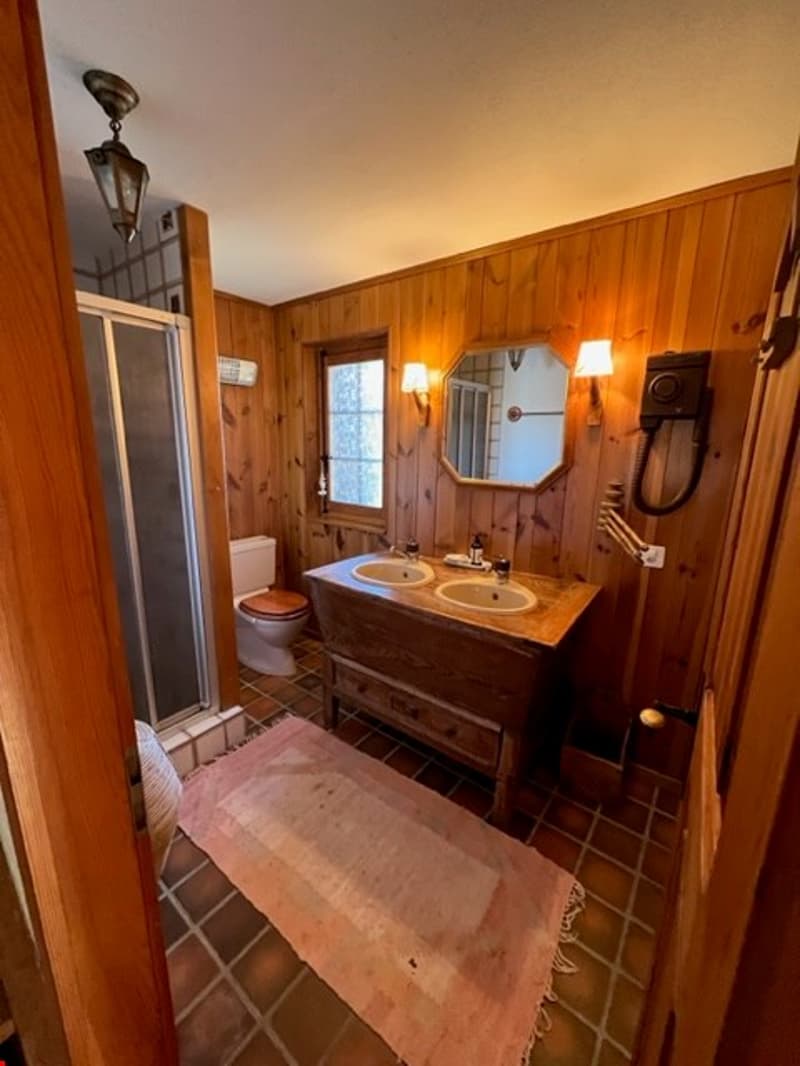 Rustic bathroom with wood paneled walls, double vanity sink, mirror, and tile flooring.