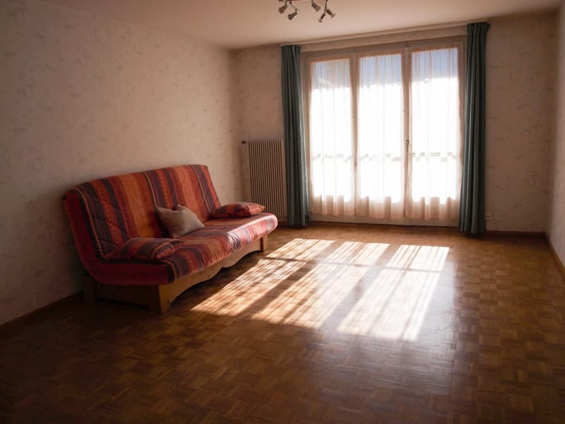 Empty room with a couch, wooden floor, large window, and a radiator