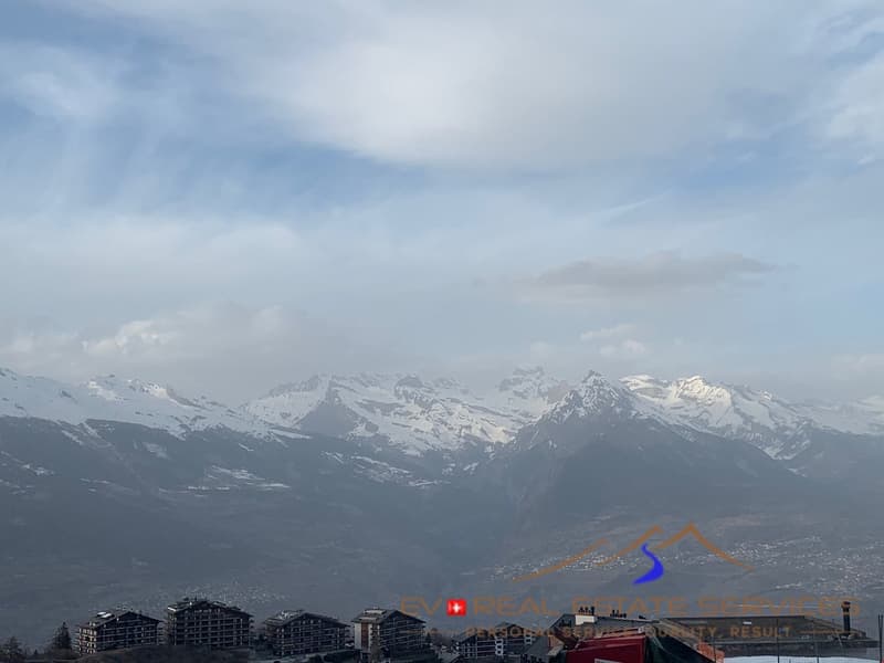 Aerial view of snowy mountains with a small town visible below, a blue sky with scattered clouds