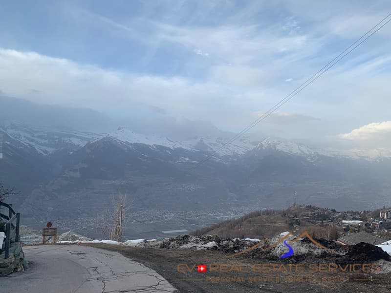 Mountainous landscape, road, city, snow-covered mountains, buildings, blue sky