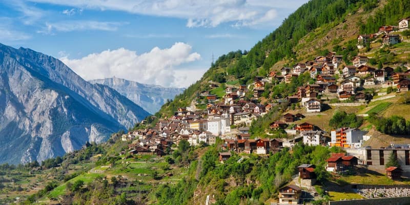 hillside village, cluster of traditional wooden houses, alpine landscape, green fields