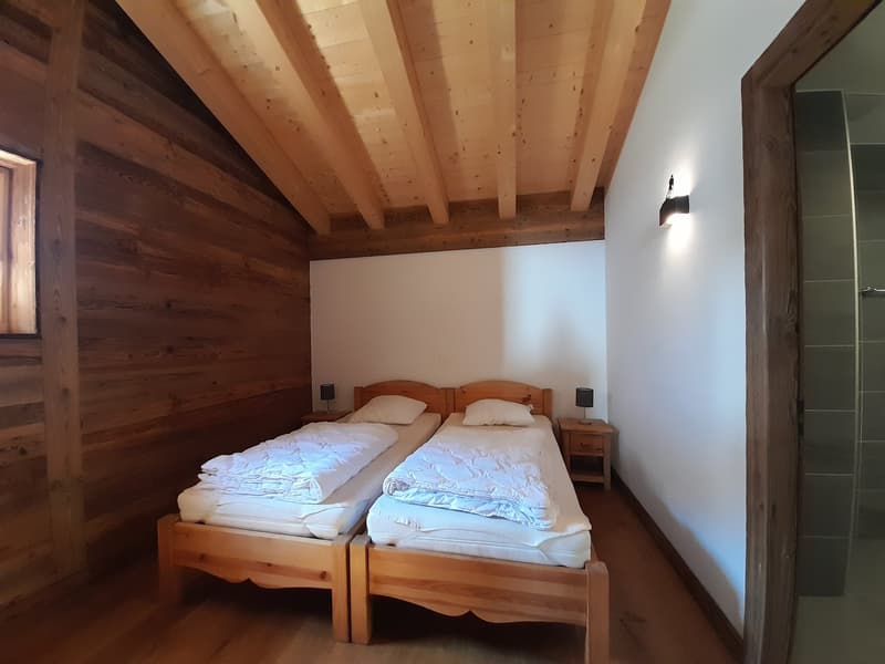 bedroom with two beds, wooden walls and ceiling, night stands, lamps, and a shower room