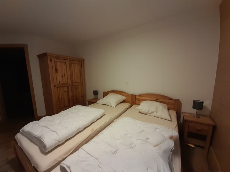 Two twin beds, wooden nightstands, lamps, a wooden wardrobe, and white bedding