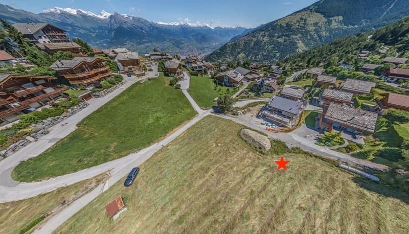 Aerial view of alpine village with mountain range in the background and plot of land marked for construction
