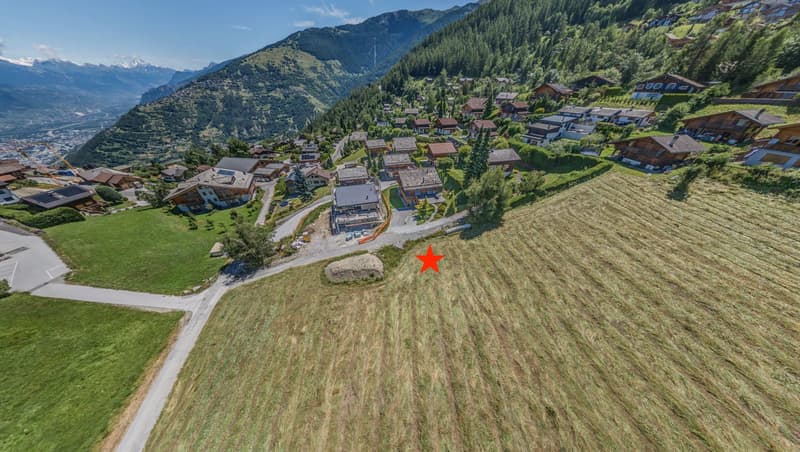 Wide open area with multiple chalets at back, mountainous background, road leading into area.