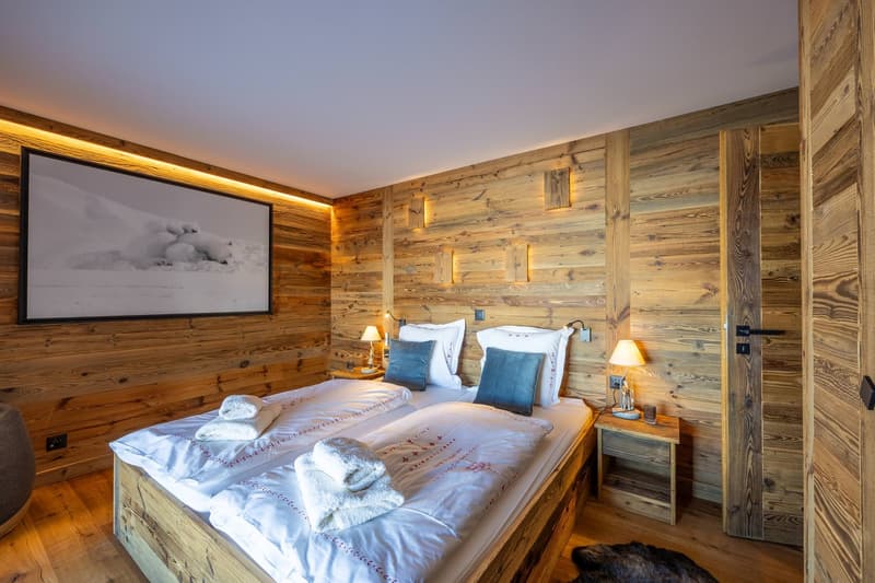Double bed, wooden walls, lamps on nightstands, rug, framed picture, floor power outlets
