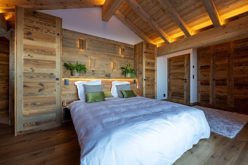 Bedroom with wooden walls and ceiling, large bed, pillows, plants on headboard, carpet
