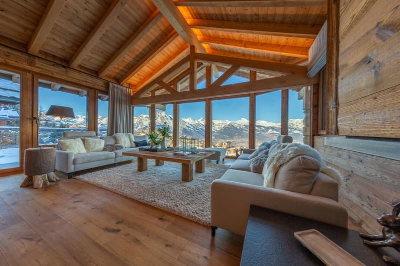 exposed wooden beams, wooden walls, large windows, beige couches, coffee table, rug, wooden floor, decorative items, snow view