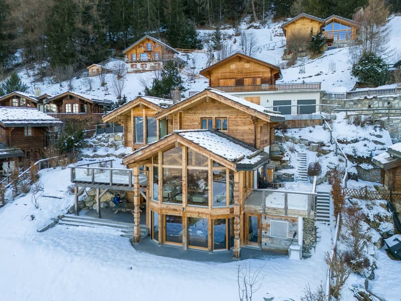 wooden house, terrace, snow on roof, windows, stone foundation, steep hill, surrounding houses