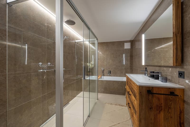 Walk-in shower, bathtub, vanity with sink, mirror, wooden storage cabinet, tiled flooring, modern fixtures, flower arrangement