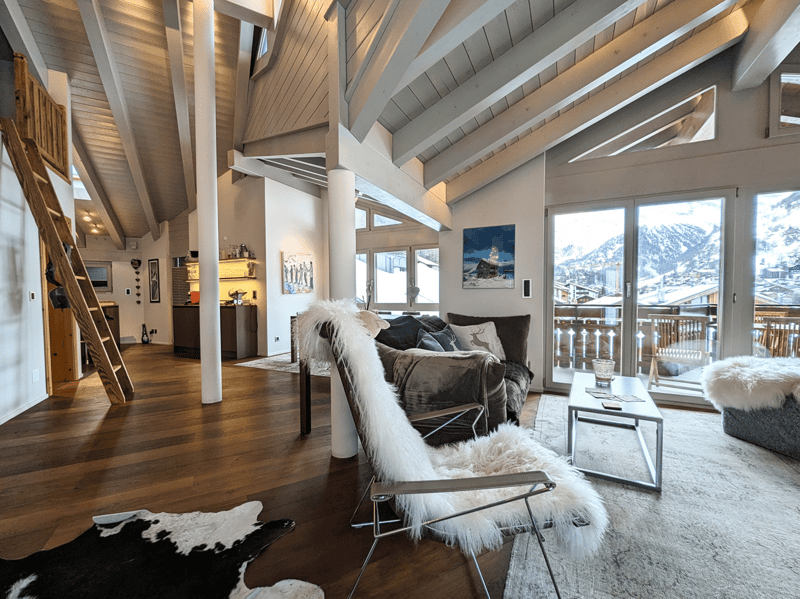 living room, exposed beams, open design, balcony, white walls, glass sliding door, wooden floor, brown sofa, wooden ladder