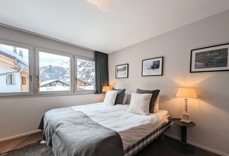 Bedroom with large windows, bed, pillows, lamps, carpet, mountain view