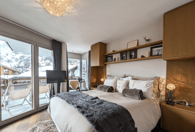 king size bed, two nightstands, two lamps, decorative items on shelves, balcony, glass walls with view