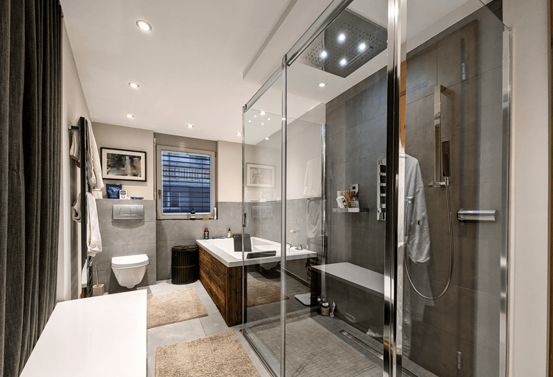 Glass shower door, bathtub, shower, window, toilet, two rugs, towels, small shelf