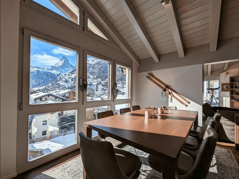 dining table with chairs, large windows, wooden ceilings, skis on the wall, mountain view