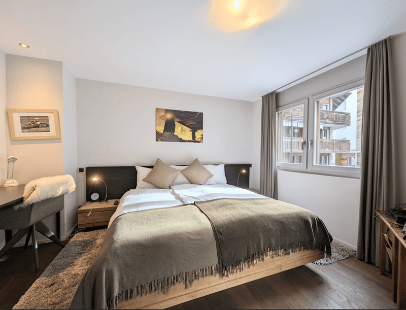 bedroom with double bed, night stand, chair, rug, paintings, desk, large window, carpeted floor