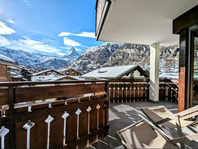 Wooden balcony, wooden lounge chairs, railing, sun, snow-capped mountains in background