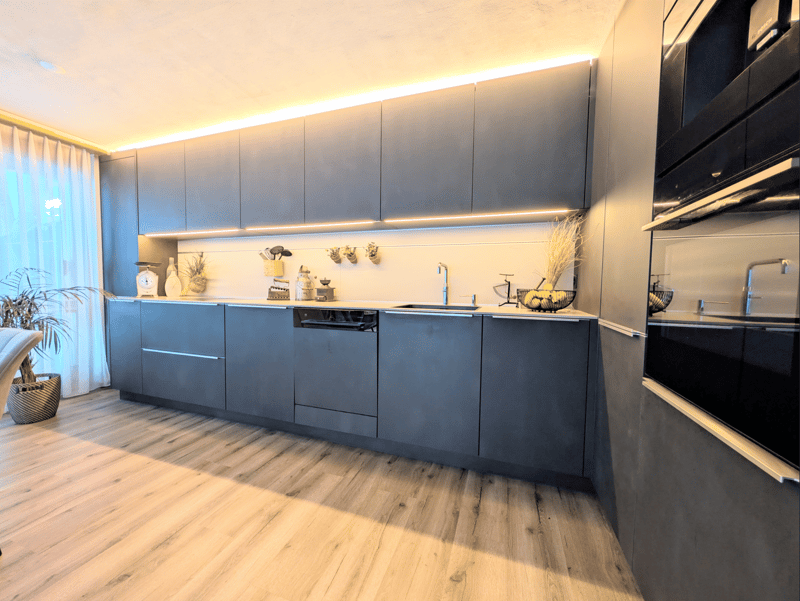 modern kitchen with wooden floor, gray cabinets, built-in dishwasher, oven, sink, faucet, countertop, decorative items