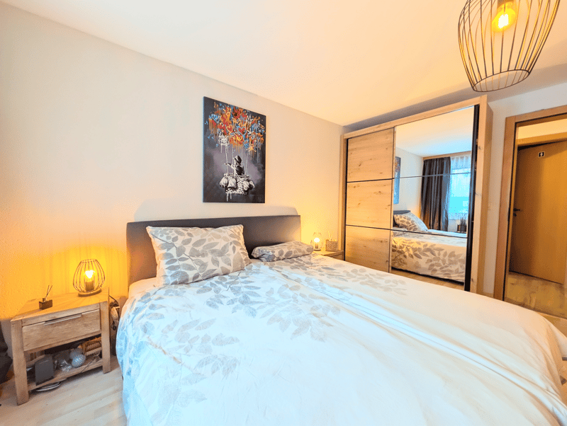 Bedroom with a double bed, nightstands, lamps, a painting, a mirror, and a wooden cabinet.
