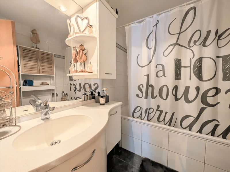 Bathroom with sink, mirror, shower curtain, shelves, and a bathtub.