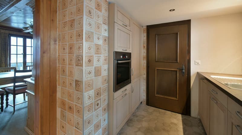 Modern kitchen with integrated appliances, patterned tiled wall, white cabinets, wooden door, and hexagon-patterned floor.