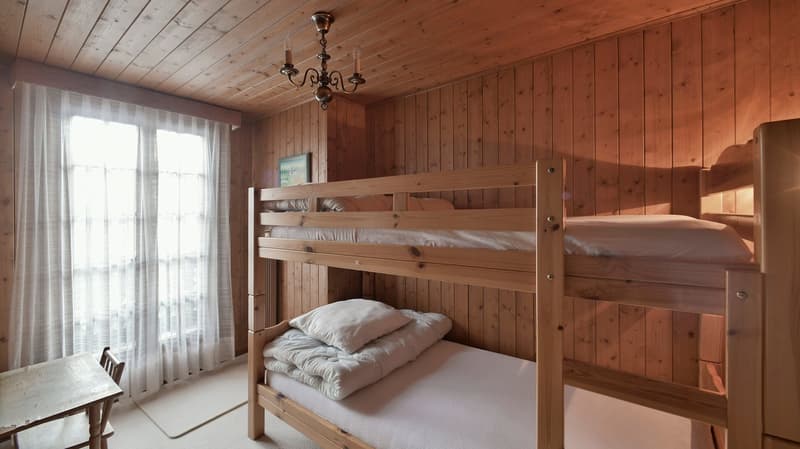A room with a wooden bunk bed and a desk with a chair next to the wall.