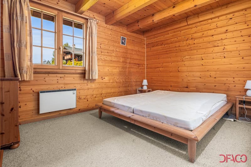 Spacious bedroom with wooden walls and ceiling, large windows, wooden bed frame, and a heater unit