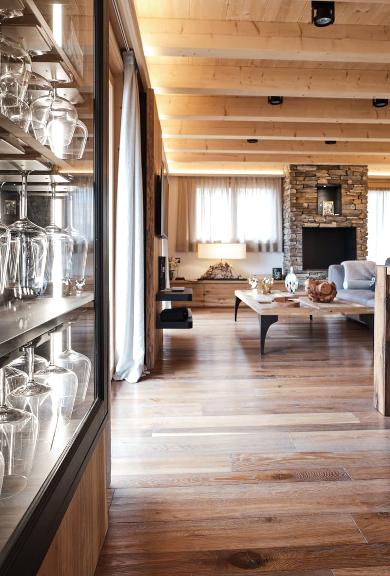 wooden floors, fireplace, couch, coffee table, wall mounted TV, shelves with wine glasses, wooden cupboards