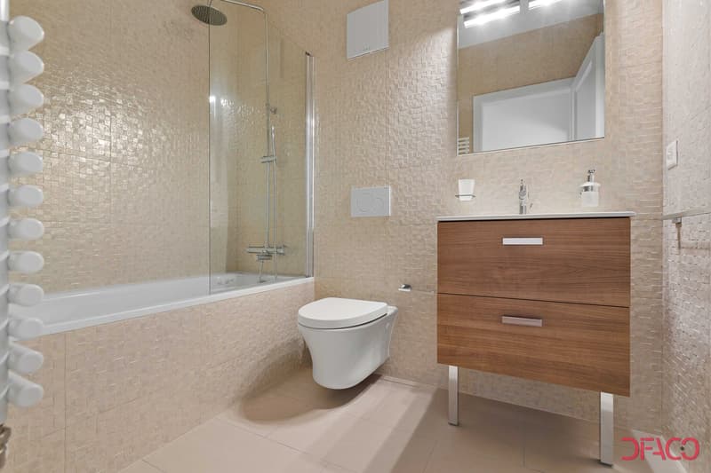 Modern bathroom with beige mosaic tile walls, a glass-enclosed shower, a white toilet, and a wooden vanity with two drawers.