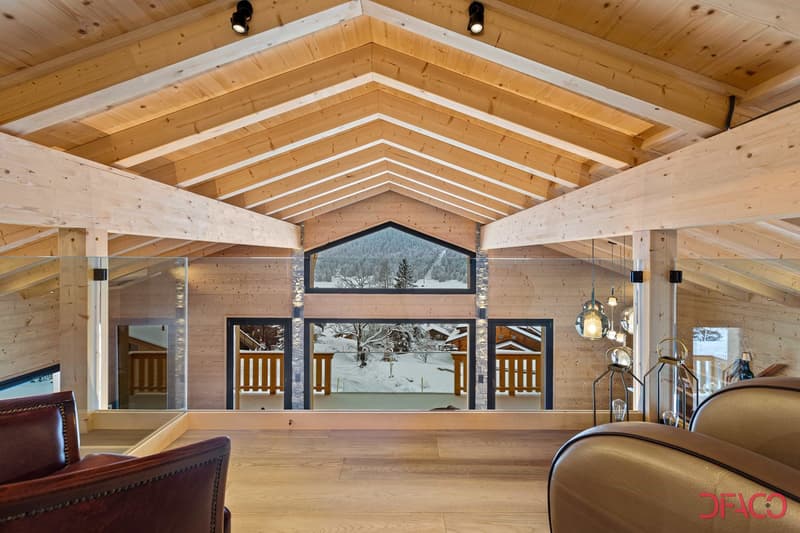 Spacious open-concept living room with high vaulted wooden ceiling, large windows offering a scenic mountain view, wooden floors, and leather furniture