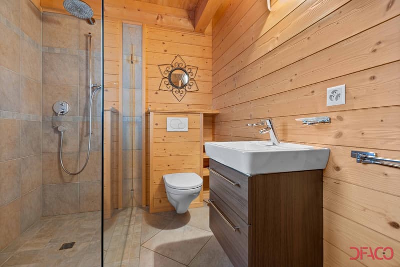 Wooden walls and ceiling, tiled floor, glass shower enclosure, vanity with sink, toilet, decorative mirror