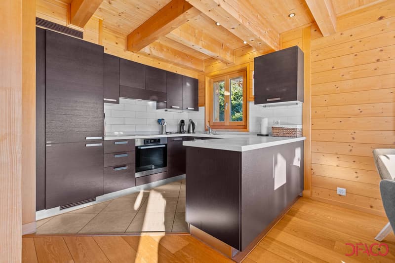 Modern kitchen with dark gray cabinets, white countertops, stainless steel appliances including a dishwasher, and a wooden ceiling with exposed beams.