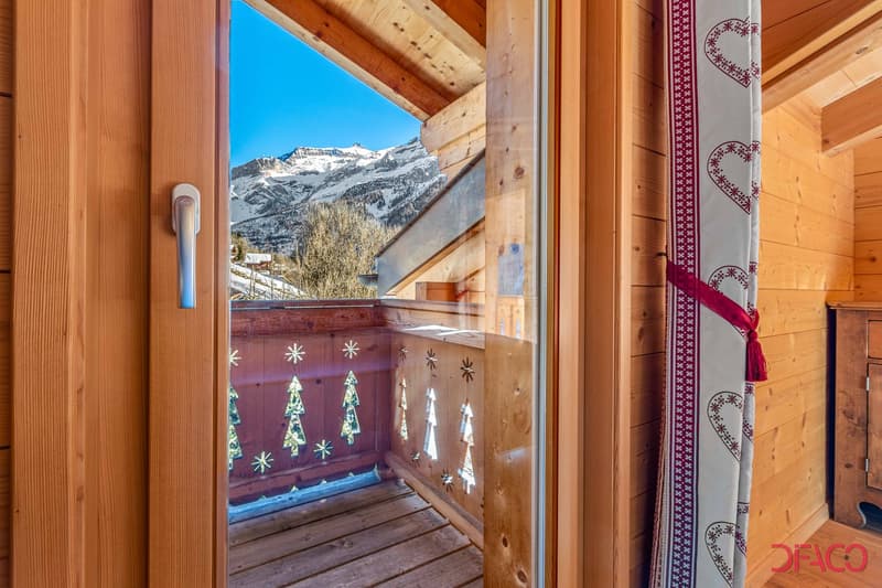 Wooden balcony with a scenic view of snow-capped mountains, decorated with Christmas-themed artwork on the walls