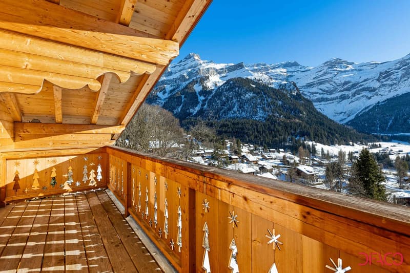 Wooden balcony with decorative snowflake patterns, overlooking a snowy mountain landscape with a village in the valley below